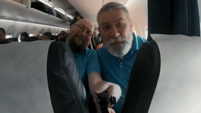 Video Reference: Facial hair, Photography, Suit, White-collar worker, Gentleman, Beard, Person, Man, Indoor, Plane, Looking, Front, Holding, Wearing, Small, Standing, Smiling, Black, Airplane, Woman, White, Suitcase, Blue, Luggage, Human face, Clothing, Glasses, Smile