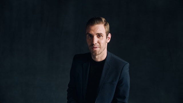 Video Reference: Face, Cheek, Head, Chin, Male, Facial hair, Standing, Portrait, Photography, Human, Person, Man, Indoor, Front, Dark, Looking, Suit, Holding, Shirt, Young, Sitting, Black, Wearing, Laptop, Table, White, Human face, Clothing, Headshot, Tie, Smile