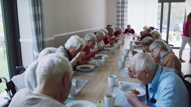 Video Reference: Meal, Lunch, Brunch, Event, Breakfast, Eating, Supper, Food, Person, Indoor, Table, Window, Sitting, People, Group, Woman, Man, Room, Front, Young, Plate, Laptop, Computer, Kitchen, White, Pizza, Standing, Living, Tableware, Human face, Clothing, Dining table