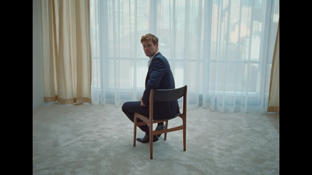 Video Reference: Sitting, Furniture, Chair, Standing, Room, Interior design, Human, Floor, Table, Window covering, Person, Indoor, Window, Looking, Building, Front, Small, White, Bed, Black, Large, Wooden, Living, Laptop, Door, Curtain, Man, Coffee table, Clothing, Couch