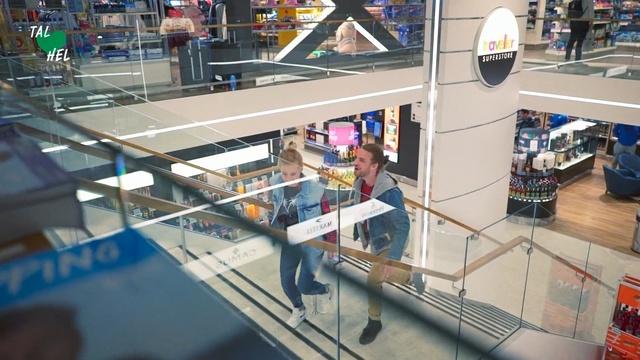 Video Reference: Shopping mall, Building, Retail, Handrail, Shopping, City, Supermarket, Person, Indoor, Table, Desk, Man, Sitting, Office, Computer, Standing, Room, Laptop, Display, Library, Holding, Kitchen, Store, Counter, Boat, White, Text, Clothing, Floor, Worktable