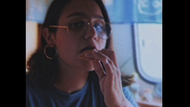 Video Reference: Face, Eyewear, Nose, Head, Mouth, Glasses, Chin, Lip, Eye, Human, Person, Indoor, Man, Sitting, Front, Window, Eating, Food, Looking, Table, Woman, Holding, Pizza, Shirt, Young, Standing, Glass, Mirror, Plate, White, Sandwich, Phone, Teeth, Human face, Clothing