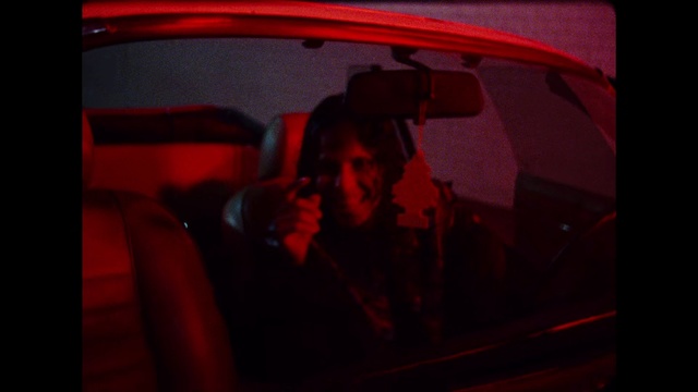 Video Reference: Red, Vehicle door, Light, Photography, Automotive lighting, Darkness, Automotive design, Vehicle, Car, Room, Person, Indoor, Sitting, Man, Table, Looking, Laptop, Front, Dark, Holding, Computer, Screen, Train, Lit, Bus, Woman, Large, Television, Standing, Mirror, Land vehicle, Auto part, Human face
