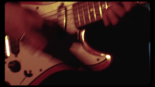 Video Reference: String instrument, Guitar, Electric guitar, Plucked string instruments, Musical instrument, String instrument accessory, Music, Musical instrument accessory, Guitarist, Indoor, Man, Table, Sitting, Monitor, Desk, Computer, Dark, Front, Holding, Hand, Keyboard, Lit, Screen, Remote, Close, Laptop, Black, Television, Mouse, Red, Control, Room, Video, Pizza, Blurry, Text, Bowed instrument