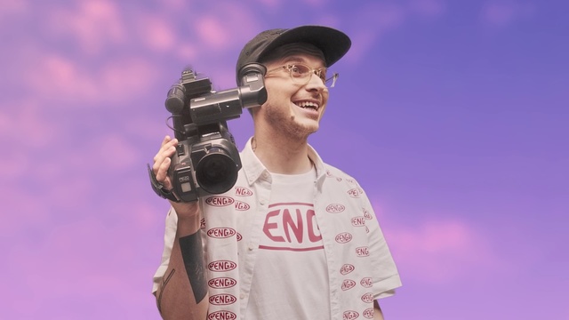 Video Reference: Music artist, Singer, Performance, Singing, Forehead, Performing arts, Music, Microphone, Photography, Talent show, Person, Outdoor, Man, Player, Wearing, Holding, Standing, Baseball, Uniform, Hat, Field, Red, Glove, Large, Phone, Ball, White, Sign, Air, Game, Sky, Camera, Human face, Clothing, Gun