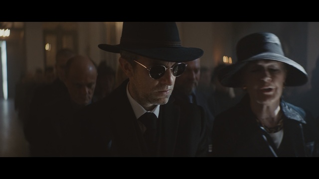 Video Reference: Fedora, Movie, Hat, Gentleman, Headgear, Darkness, Fashion accessory, Eyewear, Screenshot, Cowboy hat, Man, Person, Indoor, Clothing, Wearing, Photo, Looking, Suit, Front, Sitting, Standing, Table, Black, Woman, Dark, White, Holding, Wedding, People, Room, Human face, Glasses, Sun hat