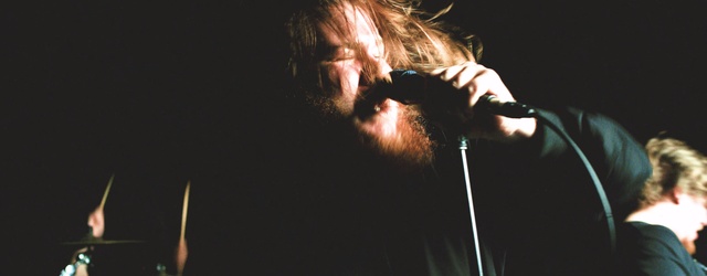Video Reference: Performance, Microphone, Singer, Musician, Microphone stand, Music, Music artist, Performing arts, Event, Singing, Person, Indoor, Man, Holding, Sitting, Looking, Front, Dark, Glasses, Black, Wine, Glass, White, Red, Young, Cake, Room, Cat, Standing, Light, Human face
