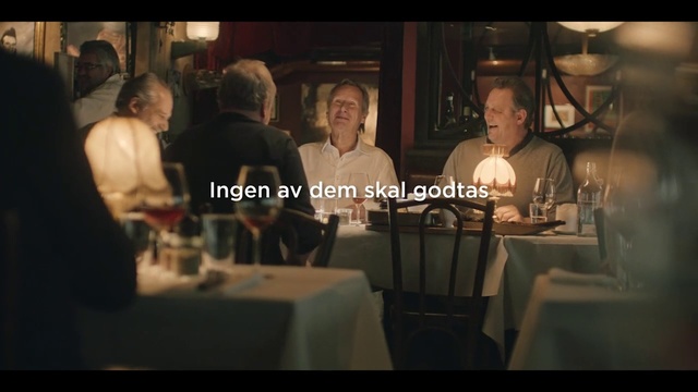 Video Reference: Conversation, Restaurant, Event, Adaptation, Photo caption, Screenshot, Drink, Movie, Person, Indoor, Table, People, Man, Group, Sitting, Woman, Front, Wine, Standing, Pizza, Large, Cake, Kitchen, Food, Young, Birthday, Holding, Eating, Room, White, Human face, Candle, Clothing, Dining table