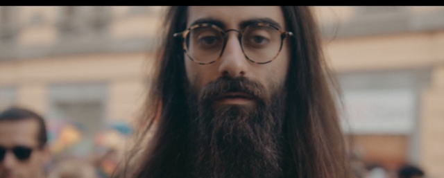 Video Reference: Facial hair, Hair, Beard, Moustache, Eyewear, Face, Glasses, Chin, Eyebrow, Head, Person, Indoor, Looking, Woman, Close, Holding, Shirt, Front, Wearing, Camera, Food, Red, Standing, Man, Sandwich, Computer, Hat, Room, Human face, Human beard, Eyes, Selfie, Portrait, Staring