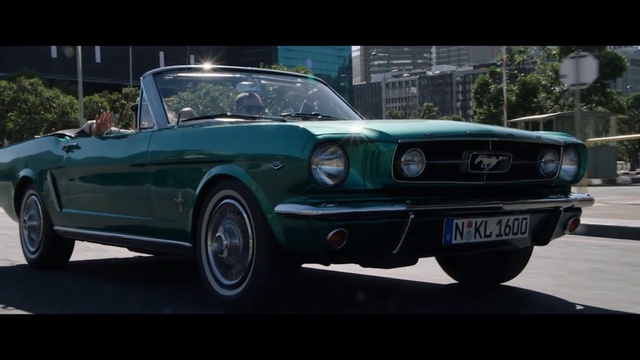 Video Reference: Land vehicle, Vehicle, Car, Classic car, Motor vehicle, Muscle car, First generation ford mustang, Sedan, Automotive design, Ford mustang, Person, Road, Outdoor, Street, Small, Green, Old, Front, Driving, City, Riding, Truck, Blue, Parked, Man, Wheel, Automotive, Auto part