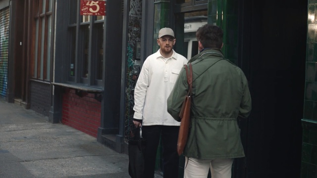Video Reference: infrastructure, road, street, standing, snapshot, outerwear, jacket, window, pedestrian, Person