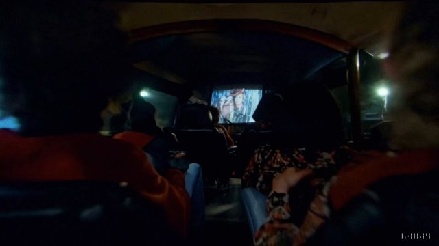 Video Reference: vehicle interior, passengers, movie screening, projector screen, night, dark scene, travel, group, view from back, screen, audience, bus, van, cinema