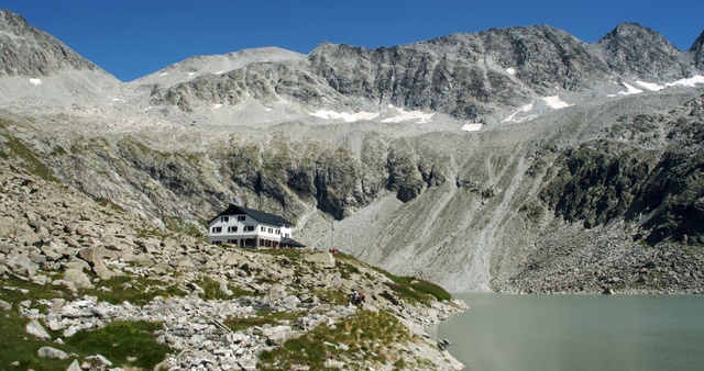 Video Reference: Mountainous landforms, Mountain, Mountain range, Highland, Hill station, Alps, Natural landscape, Geological phenomenon, Wilderness, Mountain pass, Outdoor, Nature, Snow, Rock, Rocky, Background, Man, Water, Covered, Side, Hill, Lake, Black, Standing, Riding, Green, Large, Field, White, Dirt, Air, Horse, Group, Train, Sky, Hillside