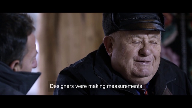 Video Reference: Movie, Human, Photo caption, Gentleman, Wrinkle, Adaptation, Screenshot, Photography, Smile, Action film, Person, Man, Looking, Indoor, Laptop, Sitting, Screen, Photo, Front, Wearing, Suit, Hat, Computer, Using, Table, Holding, Dark, Phone, Black, Glasses, Standing, Shirt, People, Room, White, Human face, Portrait, Fashion accessory, Clothing, Human beard, Text, Staring