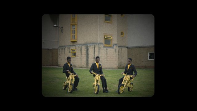 Video Reference: men, suits, bicycles, lawn, building, outdoor, yellow, group, pose, formalwear, grass, architecture, portrait, sport, novelty