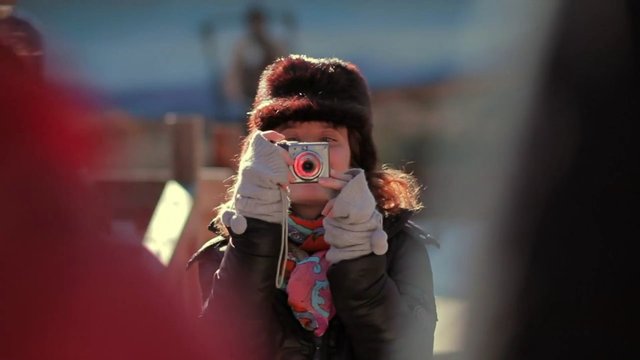 Video Reference: person, camera, photography, winter, gloves, fur hat, outdoors, portrait, taking photo, close-up, bokeh, cold weather