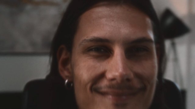 Video Reference: close-up, portrait, smiling, young man, indoors, blurred, shallow depth of field, face, headshot, casual, low light, out of focus