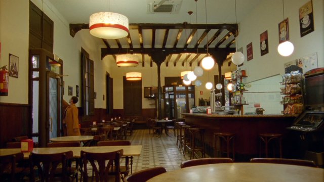 Video Reference: cafe, coffee shop, interior, empty tables, bar counter, hanging lights, vintage decor, restaurant, indoor, warm lighting, seating, person, counter, cozy, architecture, slow scene