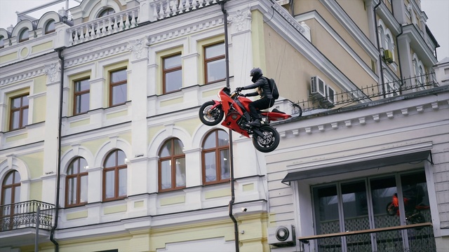 Video Reference: Footwear, Wheel, Tire, Daytime, Window, Building, Motorcycle, Vehicle, Helmet, Stunt performer