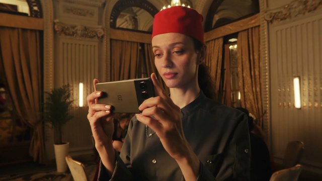 Video Reference: woman, smartphone, portrait, indoor, warm lighting, red hat, technology, mobile phone, ornate interior, close-up, person, camera phone