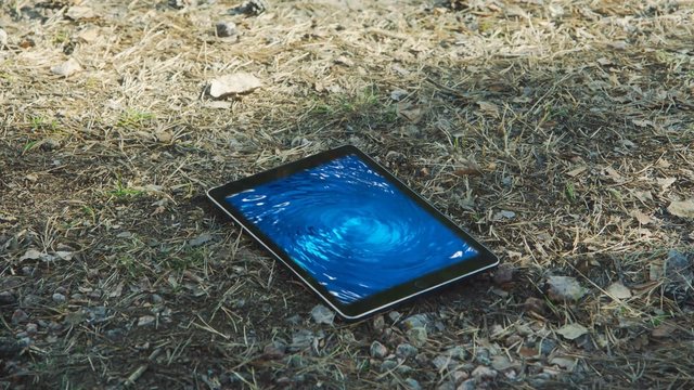 Video Reference: tablet, device, screen, outdoor, ground, grass, dry leaves, technology, blue, swirl, water effect, close-up