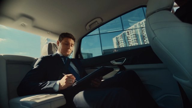 Video Reference: car interior, businessman, back seat, tablet, writing, city, urban, commute, suit, window view, luxury car, professional, travel, office, daylight