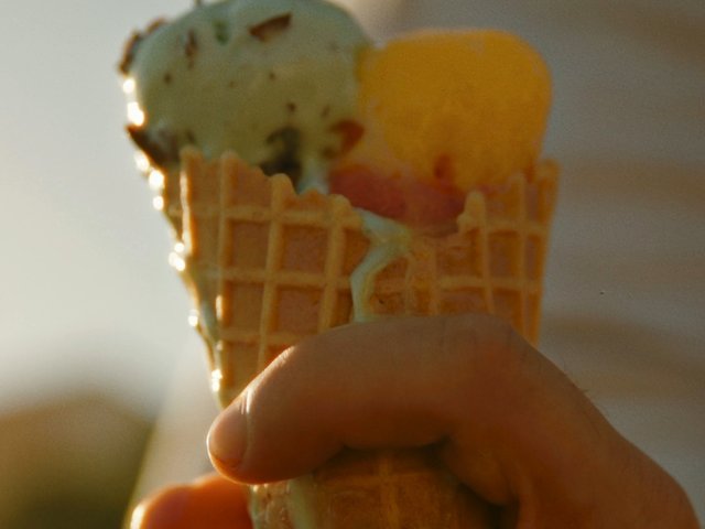Video Reference: ice cream, cone, dessert, hand, close-up, sunlight, warm light, food, summer, sweet, frozen dessert, waffle cone, outdoor, blurred background