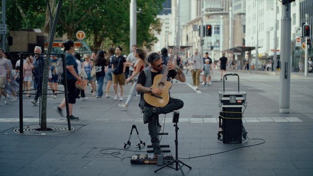Video Reference: street musician, guitar, busker, sidewalk, city street, urban, pedestrians, live music, outdoor, performance, acoustic guitar, crowd, public space, street performance