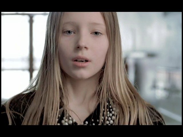 Video Reference: girl, child, close-up, portrait, blonde hair, indoors, looking at camera, blurry background, neutral expression, daylight