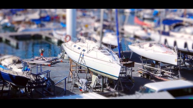 Video Reference: sailboat, boatyard, marina, yacht, maintenance, repair, dry dock, boats, harbor, sailing, shipyard, storage, person, outdoors, waterfront, blurred