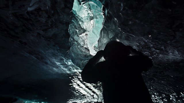 Video Reference: ice cave, silhouette, person, dark, blue ice, glacier, cave interior, frozen, reflection, adventure, exploration, nature, low light, rock, winter