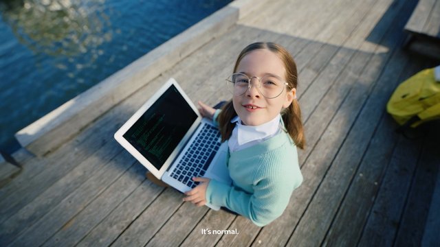 Video Reference: child, girl, glasses, laptop, dock, water, outdoor, smiling, technology, education, wooden deck, top view, subtitle, screen, casual, daylight