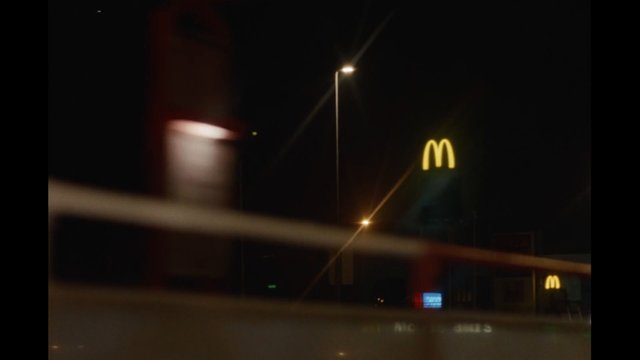 Video Reference: night, street, streetlights, fast food, restaurant, signage, urban, blurred foreground, dark, building exterior, roadside, nightscape