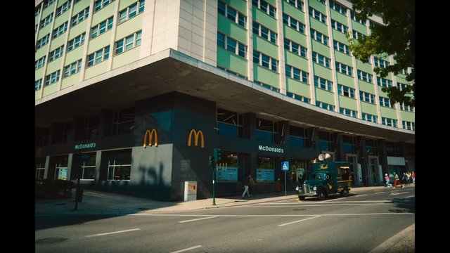 Video Reference: street, building, urban, McDonalds, storefront, road, pedestrians, truck, corner, city, architecture, daytime, exterior, restaurant, vehicle