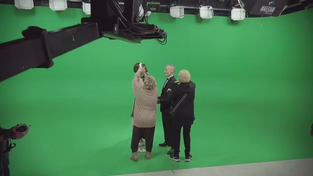 Video Reference: Coat, Green, Camera, Videographer, Gesture, Film studio, Suit, Video camera, Cameras & optics, Tripod
