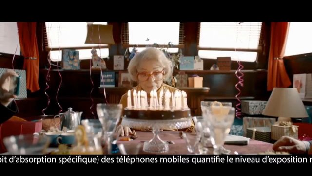 Video Reference: elderly woman, birthday, birthday cake, candles, party table, gifts, indoor, celebration, family gathering, subtitle, home interior, glassware, decorations, warm lighting