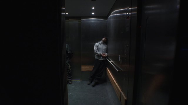 Video Reference: elevator, interior, dim light, person, standing, leaning, metal walls, indoor, dark, reflection, transportation