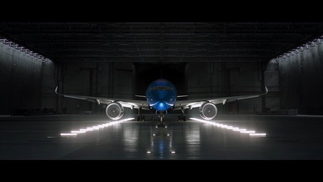 Video Reference: airplane, jet, hangar, airport, commercial aircraft, front view, blue nose, landing gear, engine, wings, indoor, runway lights, reflection, dark interior, aviation