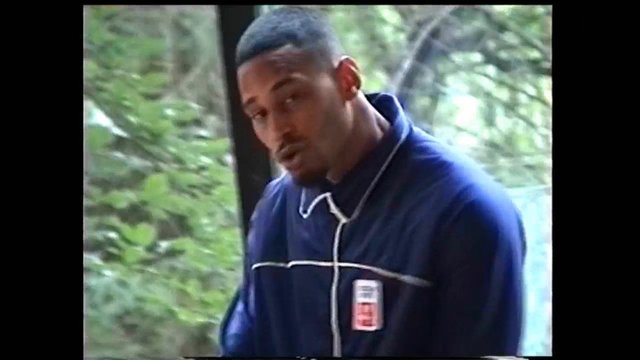 Video Reference: man, portrait, outdoors, trees, greenery, blue tracksuit, close-up, blurred background, casual clothing, standing, daylight