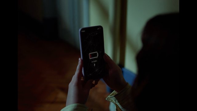 Video Reference: smartphone, low battery, cracked screen, handheld, indoors, dim lighting, mobile phone, technology, battery warning, screen damage, close-up, person, device
