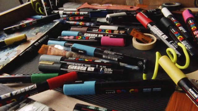 Video Reference: paint markers, art supplies, markers, drawing tools, tabletop, clutter, workspace, palette, masking tape, craft, stationery, assorted tools, close-up, still life