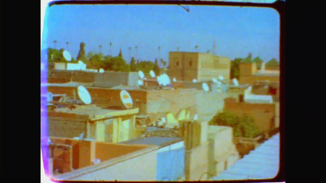 Video Reference: urban, rooftops, satellite-dishes, buildings, neighborhood, cityscape, residential, sky, daytime, distant-view, low-resolution, outdoor