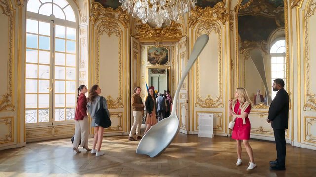 Video Reference: gallery, museum, ornate interior, gilded room, chandelier, sculpture, oversized spoon, visitors, art exhibit, historic interior, interior design, luxury, tourism, people, french style
