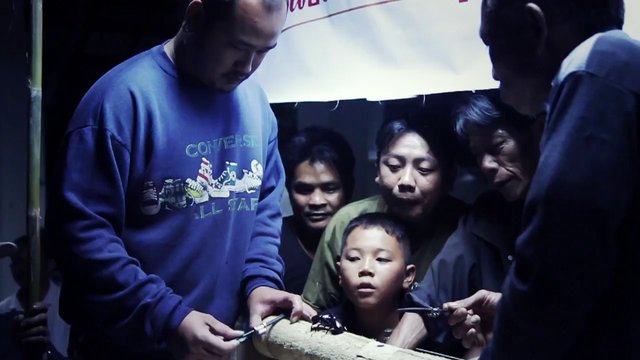 Video Reference: people, group, child, indoor, dim light, close up, gathering, family, observation, bamboo, night, community, standing, interaction