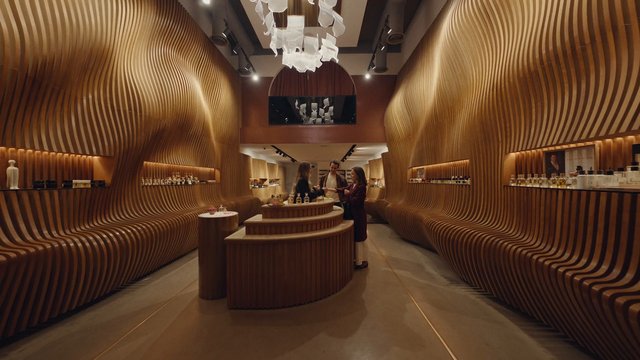 Video Reference: luxury interior, showroom, boutique, wood paneling, modern design, interior architecture, retail display, bottles, counter, people, warm lighting, sophisticated, curved walls, ambient lighting, store, elegant
