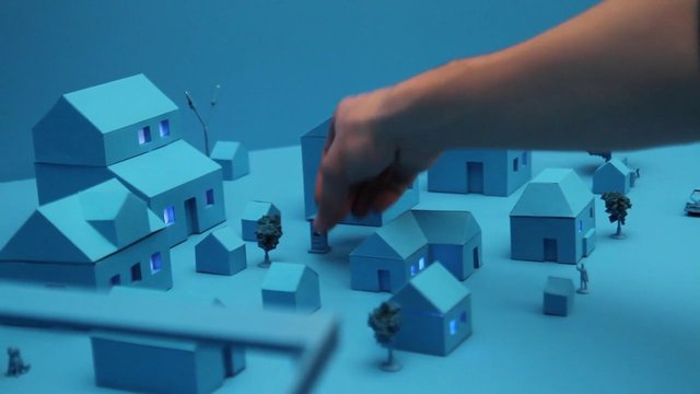 Video Reference: miniature, model village, houses, hand, neighborhood, tabletop, blue lighting, architecture, toy town, scale model, urban planning, miniature trees