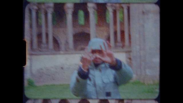 Video Reference: person, hoodie, outdoors, standing, hands up, building, grass, blurry, grainy, low light, portrait, urban