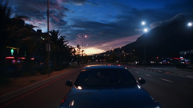 Video Reference: car, driving, road, dusk, sunset, city street, streetlights, mountains, palm trees, nightfall, urban, travel, motion blur, sky, landscape