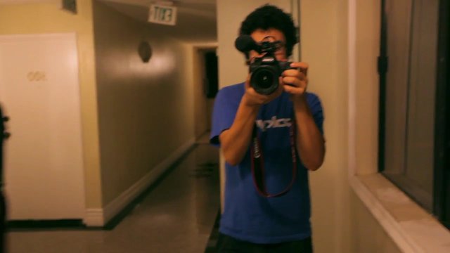 Video Reference: person, camera, videographer, filming, hallway, mirror, indoor, portrait, blue shirt, home interior