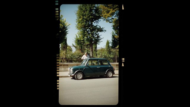 Video Reference: car, vintage, hatchback, street, parked, trees, fence, sidewalk, daylight, outdoors, urban, person, road, classic car